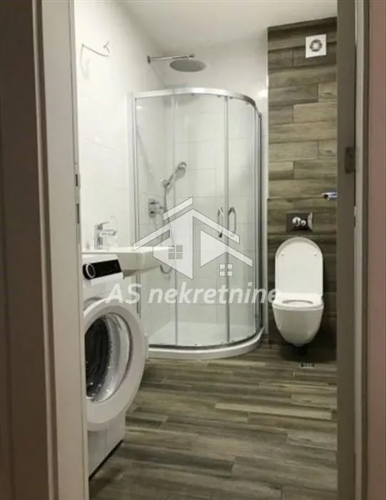 Moderno kupatilo sa tuš kabinom, konzolnom šoljom i veš mašinom.