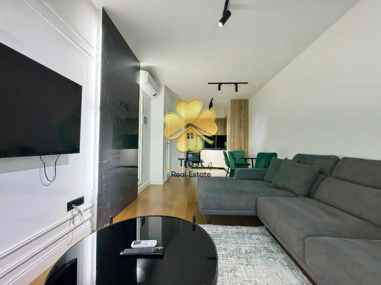 Modern living room with a sofa, TV, and view of the dining area and kitchen.