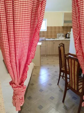 View from the room towards the kitchen with a dining table and red and white curtains. - image 3