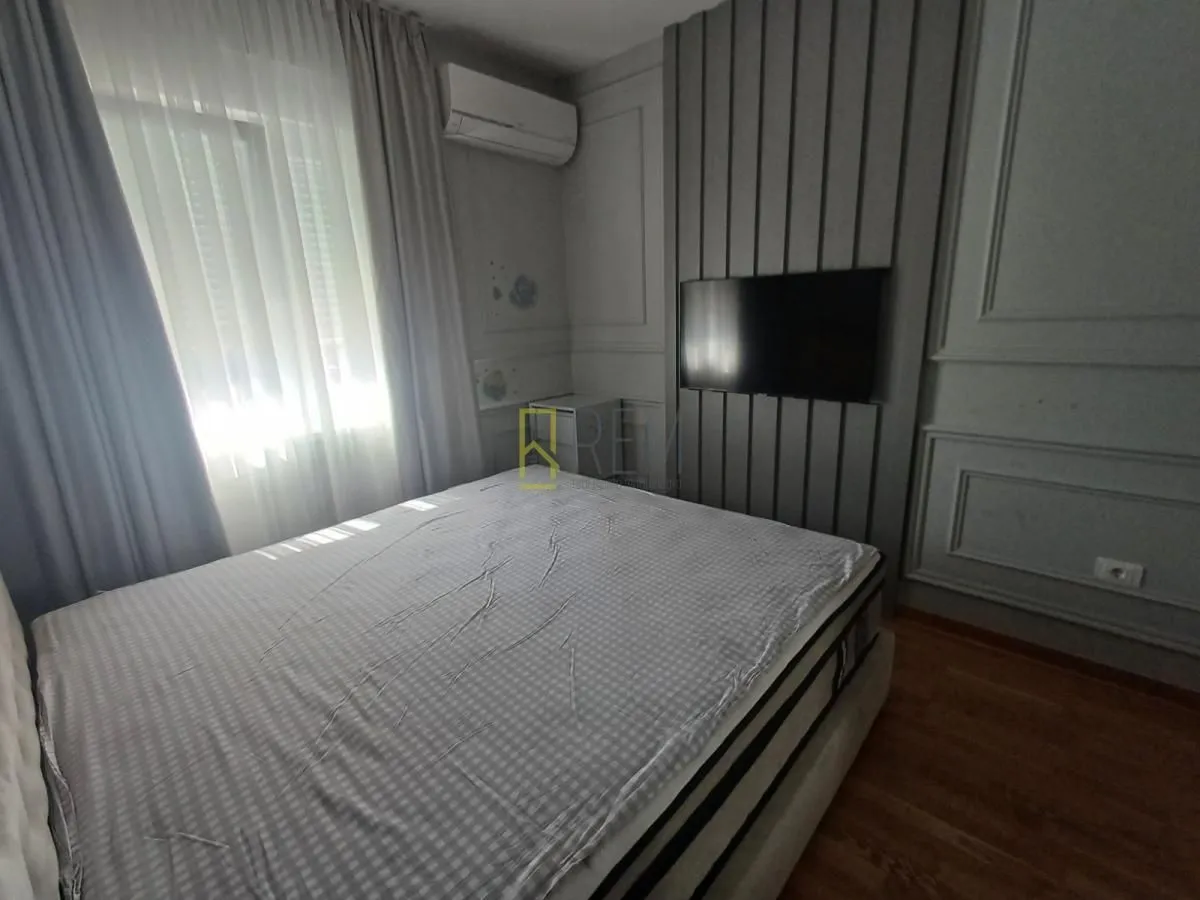 Moderna spavaća soba sa bračnim krevetom, TV-om na zidu i klima uređajem.