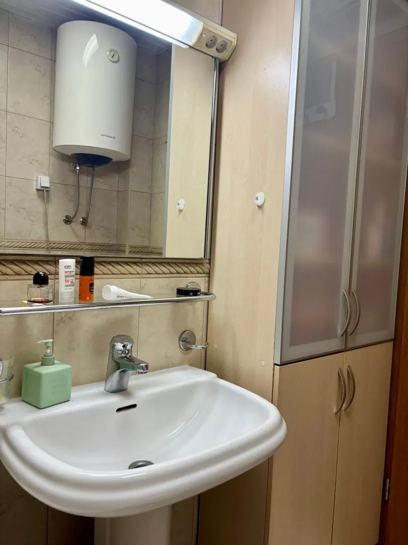 Bathroom with a sink, mirror, water heater, and wooden cabinet.