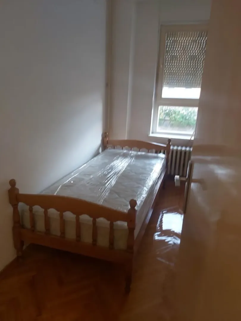 Manja spavaća soba sa drvenim krevetom i parketom.