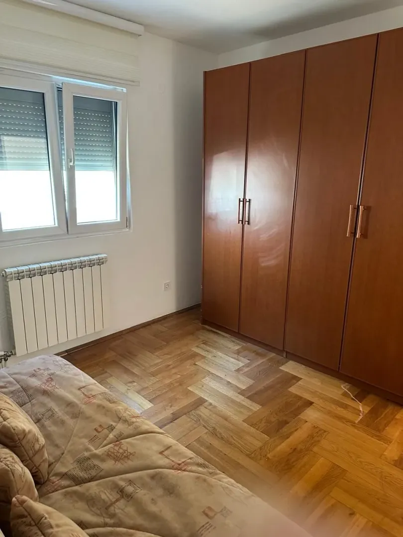 Smaller bedroom with a large wooden wardrobe, bed and parquet flooring.