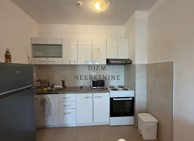 Manja bijela kuhinja sa kuhinjskim elementima i frižiderom.