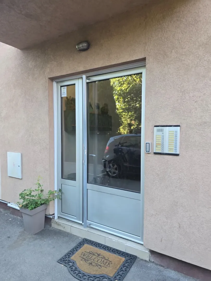 Ulaz u stambenu zgradu sa staklenim vratima i interfonom.
