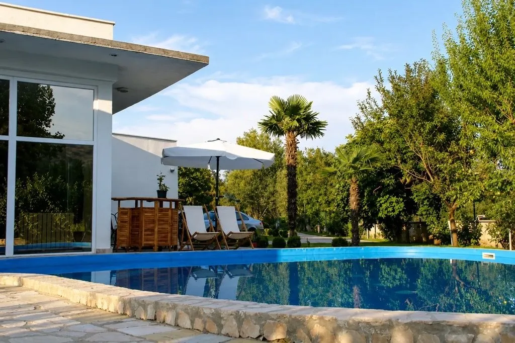 Yard with a swimming pool and sun loungers in front of a modern house.