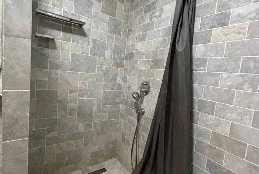 Pogled na tuš kabinu obloženu kamenim pločicama sa tamnom zavjesom.