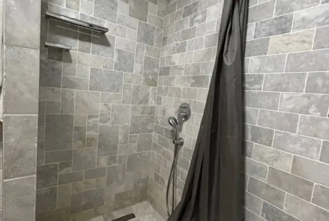 Pogled na tuš kabinu obloženu kamenim pločicama sa tamnom zavjesom. - image 16