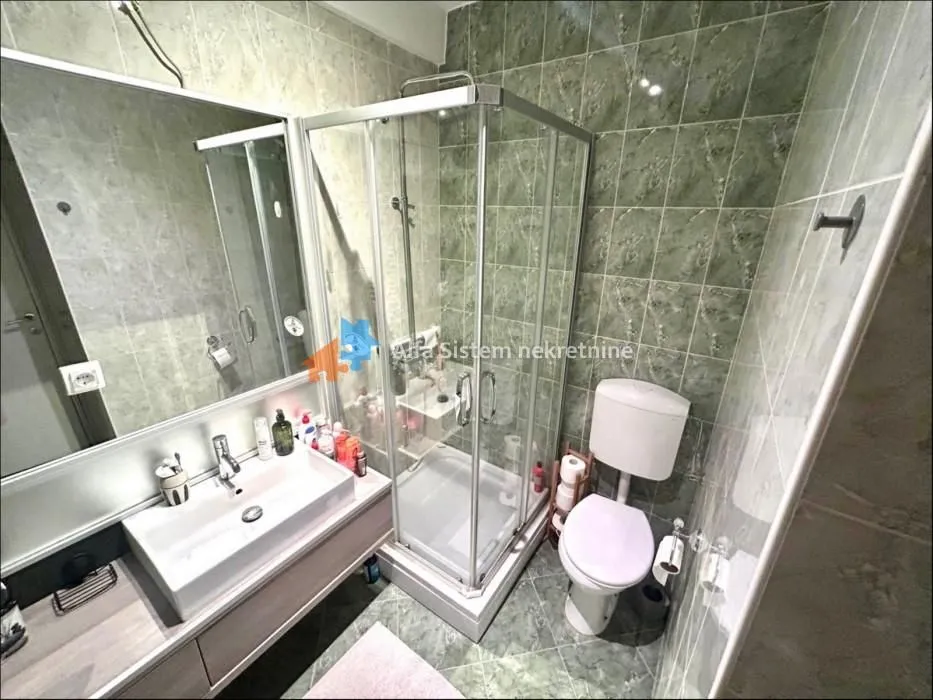 Bathroom equipped with a shower cabin, washbasin, and toilet with green ceramic tiles.