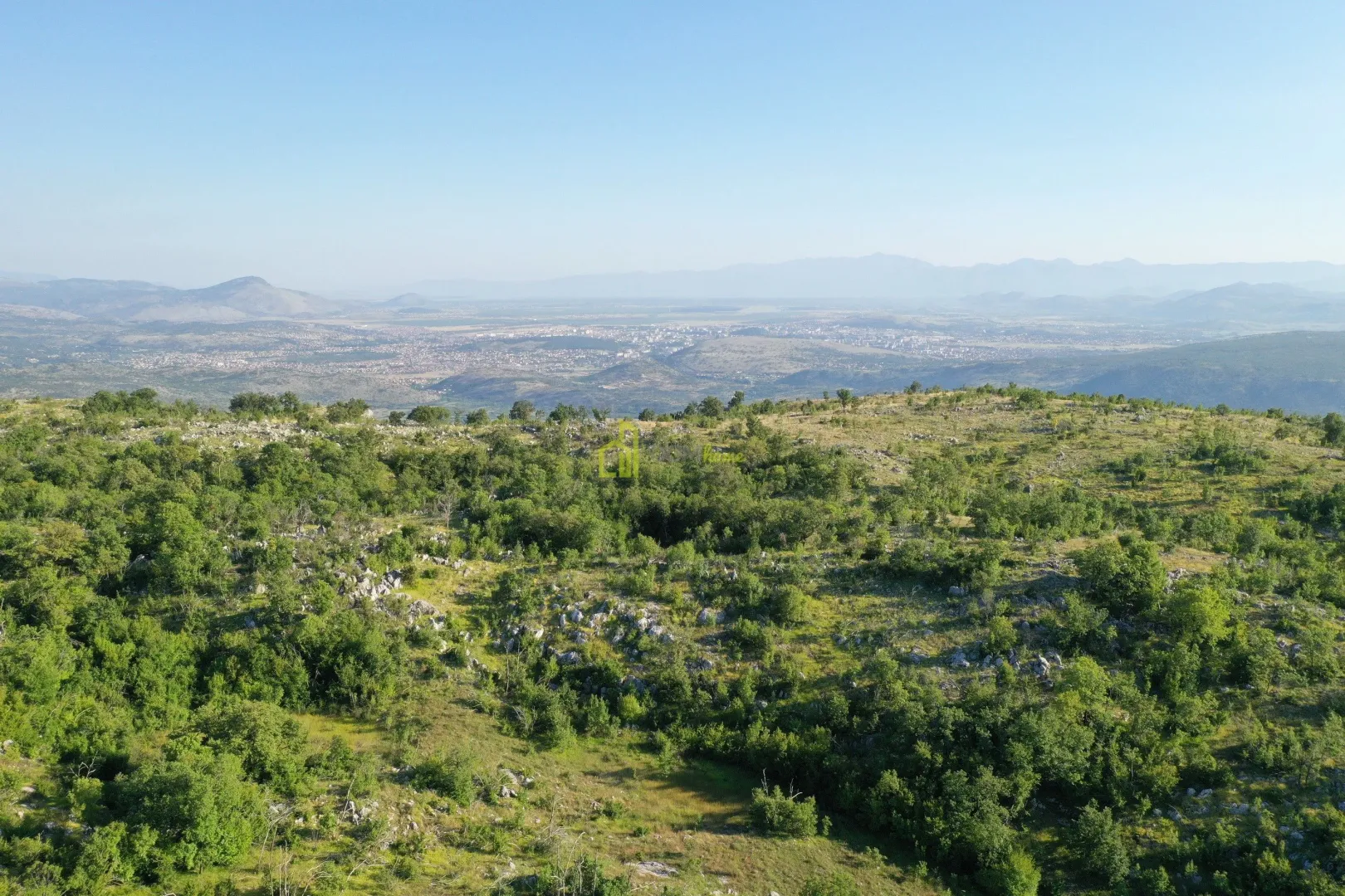 Pogled iz vazduha na šumoviti pejzaž sa gradom u daljini.
