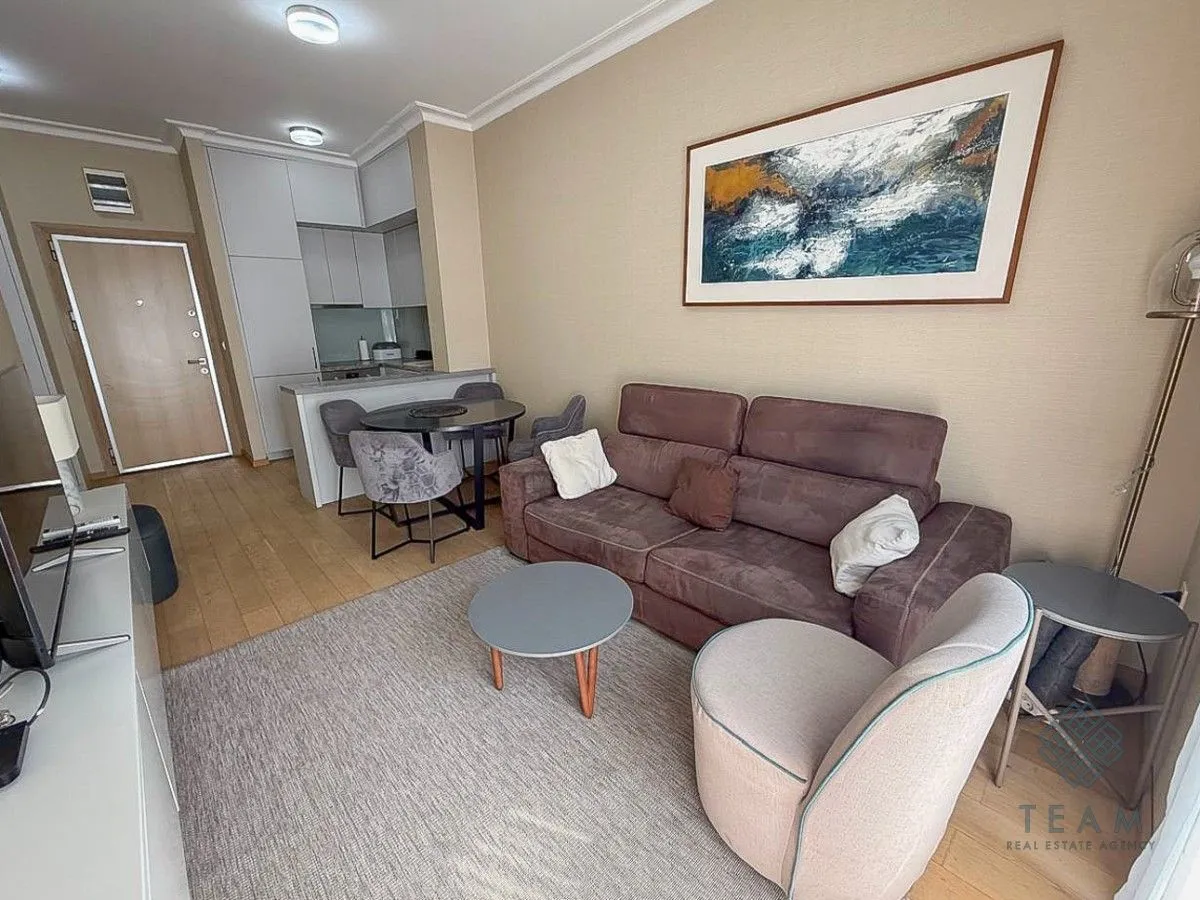 Living room with a sofa set, dining table and kitchen in the background.