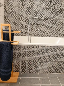Bathroom with a mosaic-tiled bathtub and a wooden towel rack. - image 11