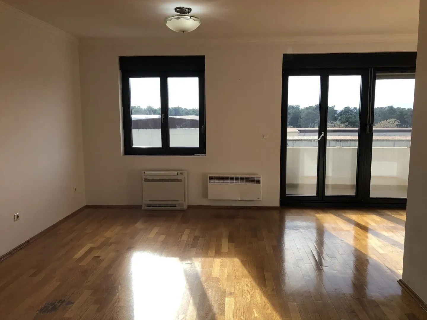 Empty room with parquet flooring, windows, and balcony doors.