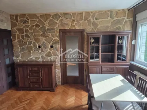 Dnevna soba sa drvenim nameštajem i zidom obloženim kamenom. - image 3