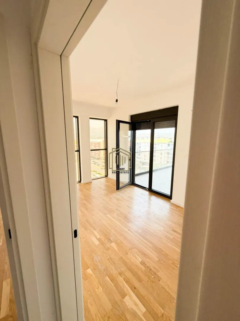 View from the hallway into an empty room with wooden flooring and access to the terrace.