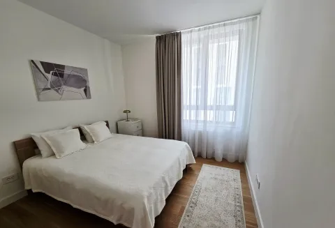 Svetla spavaća soba sa bračnim krevetom, noćnim stočićem i prozorom prekrivenim zavesama. - image 8
