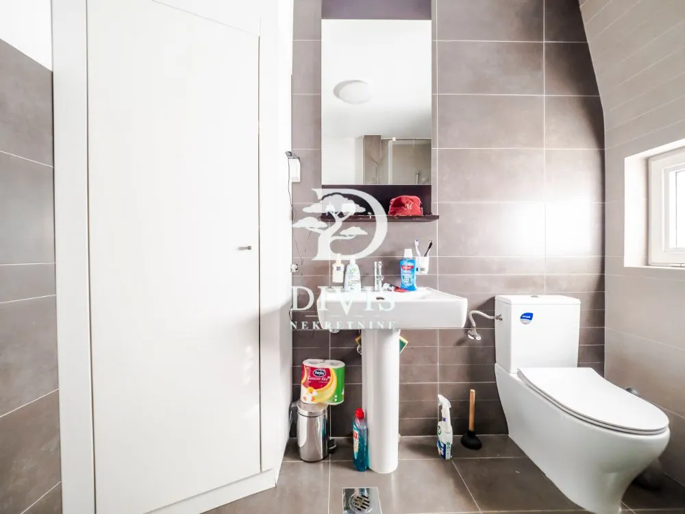 Bathroom tiled in grey with a washbasin and toilet.