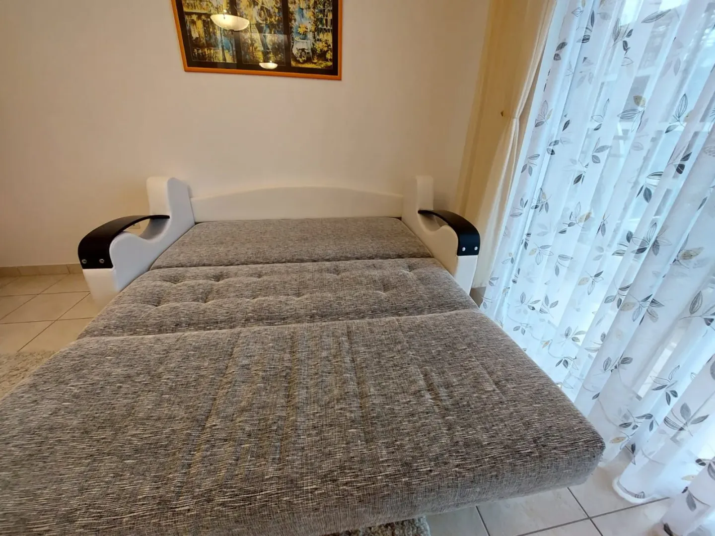 Spavaća soba sa krevetom na rasklapanje i prozorom sa zavjesom.