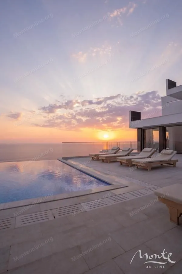 Terrace with a swimming pool and sun loungers overlooking the sea at sunset.