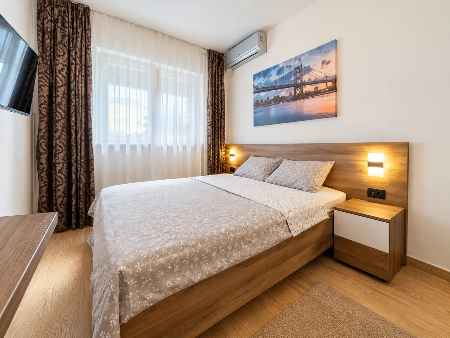 Furnished bedroom with a double bed, bedside tables, and a wall-mounted TV.