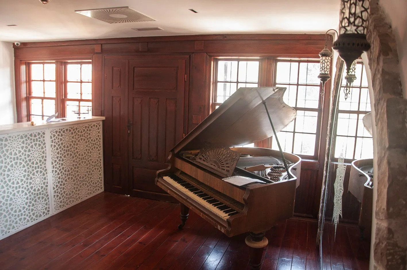 Living room with wooden flooring, a piano, and large windows.