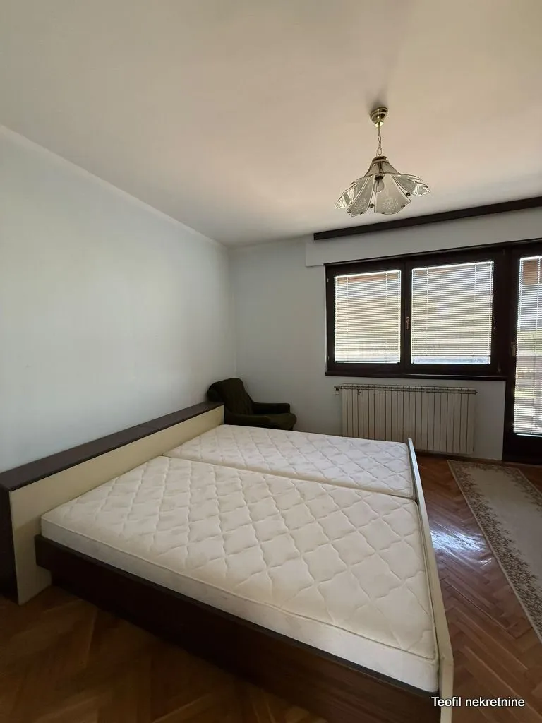 Spavaća soba sa bračnim krevetom, foteljom i prozorom.