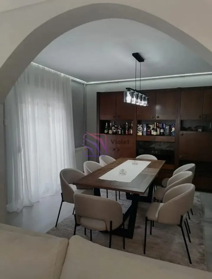 Trpezarija sa velikim drvenim stolom i stolicama u sklopu dnevnog boravka.
