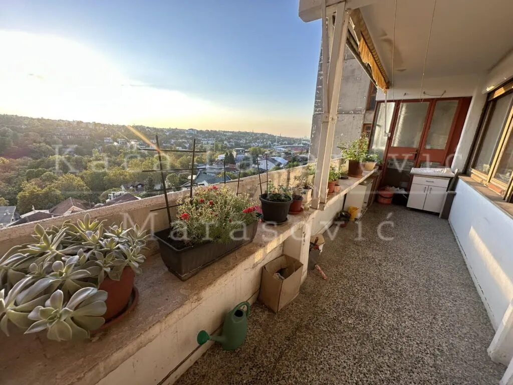 Prostrani natkriveni balkon sa saksijama cveća i pogledom na grad.