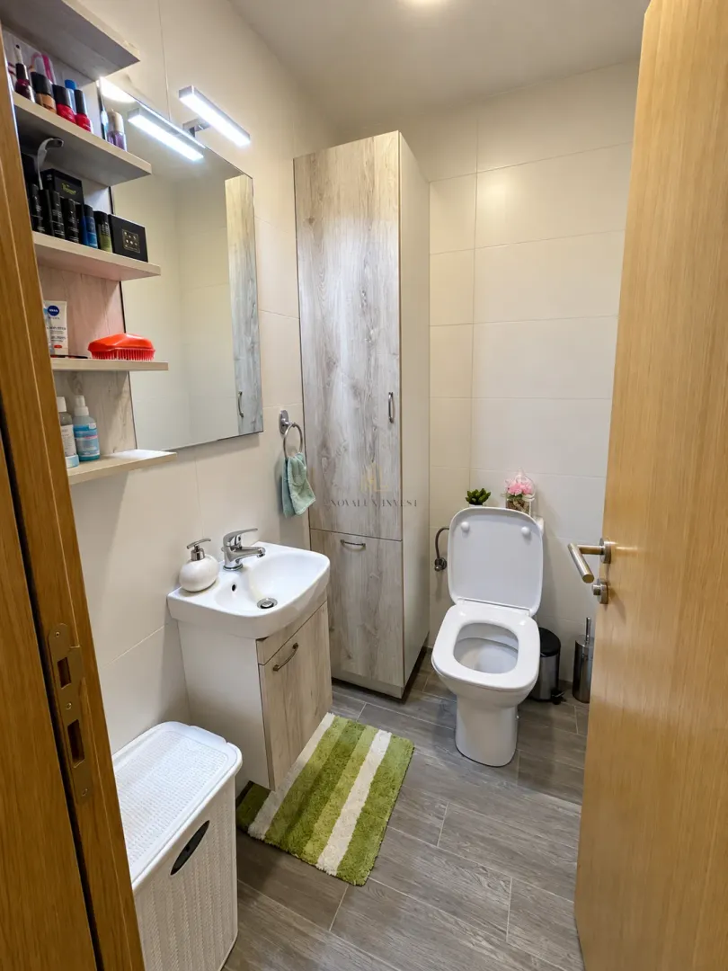 Kupatilo sa umivaonikom, ogledalom, wc šoljom i visokim ormarićem.