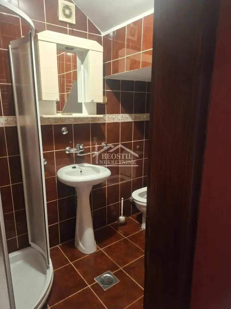 Small bathroom tiled in brown with a shower cabin, washbasin, and toilet.