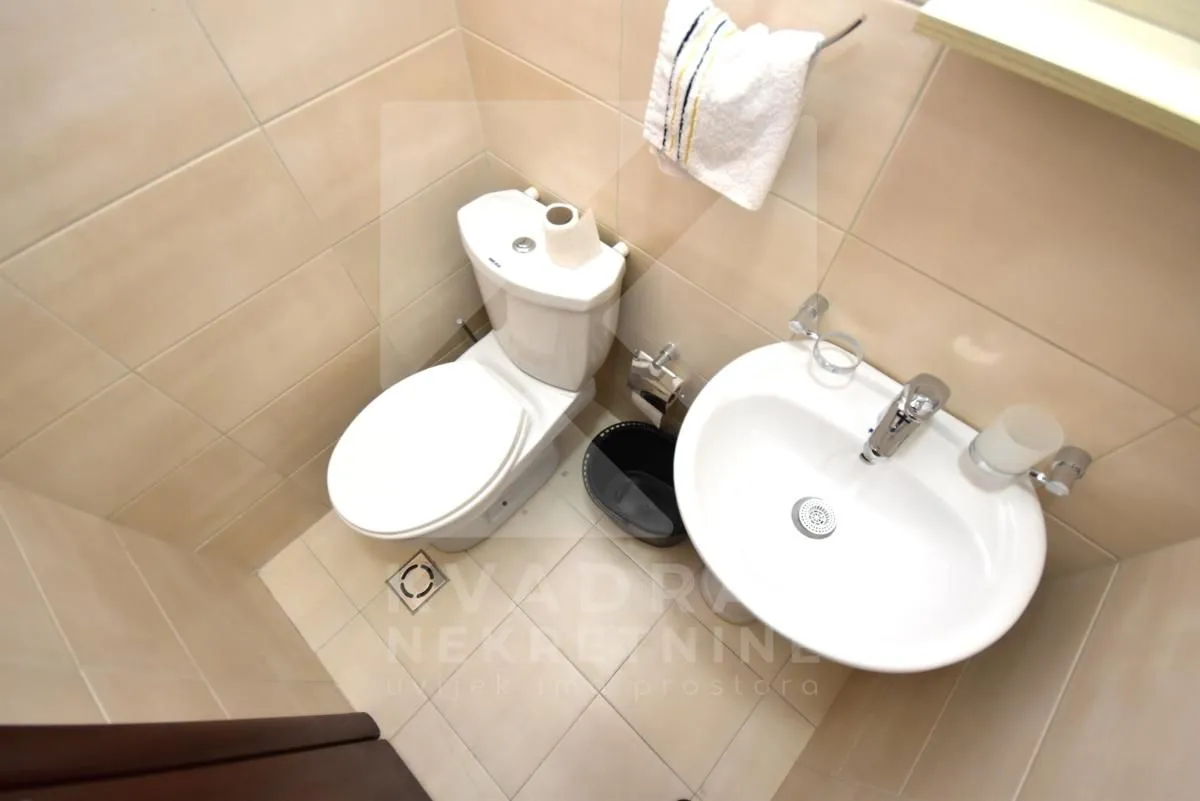 Manje kupatilo sa wc šoljom i umivaonikom obloženo keramičkim pločicama.