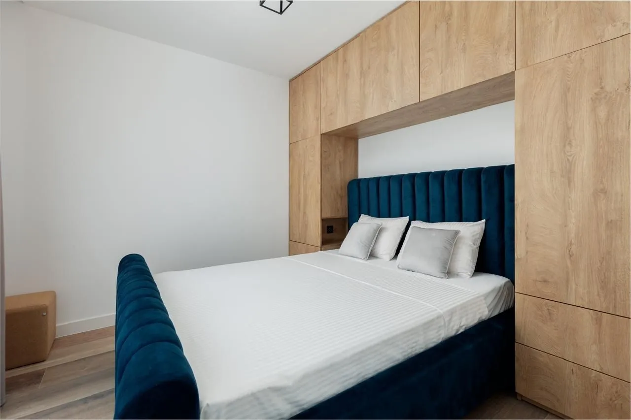 Bedroom with a blue upholstered bed and built-in wooden wardrobes.