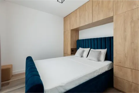 Bedroom with a blue upholstered bed and built-in wooden wardrobes. - image 2