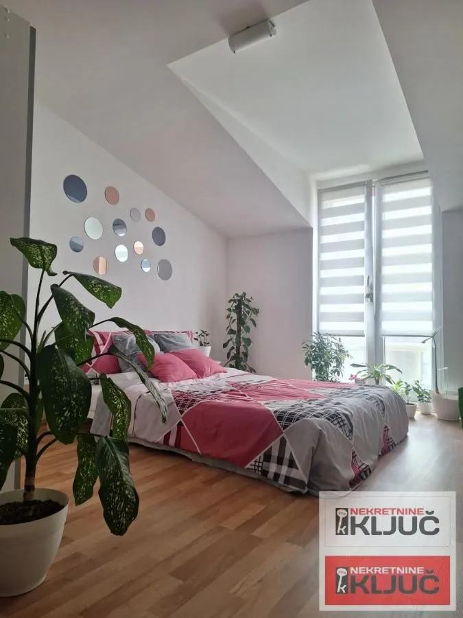 Svetla spavaća soba sa bračnim krevetom, drvenim podom i ukrasnim ogledalima na zidu.