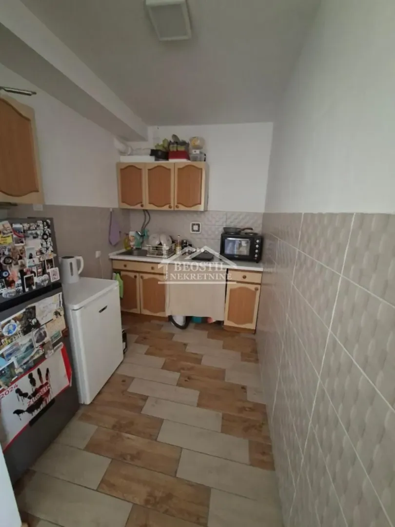 Manja kuhinja sa drvenim elementima, frižiderom i mikrotalasnom pećnicom.