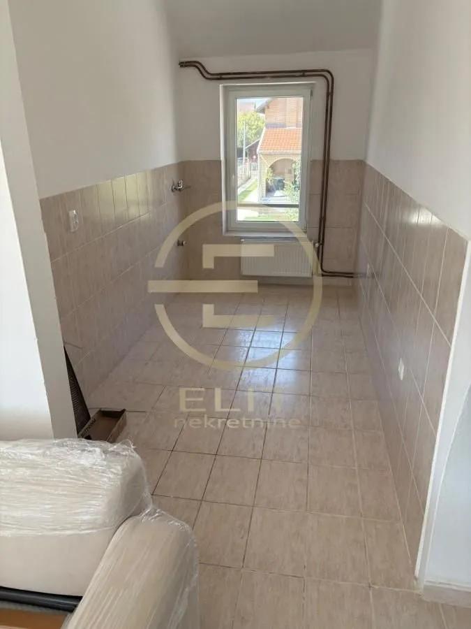 Empty kitchen with tiled floor and walls and a window at the end.