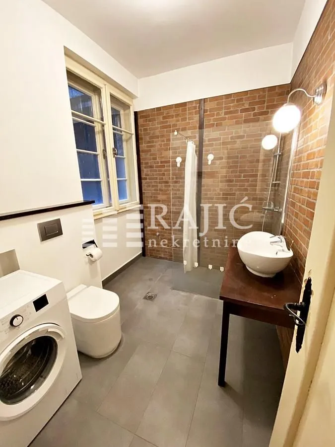 Modern bathroom with a walk-in shower, washbasin, and washing machine.