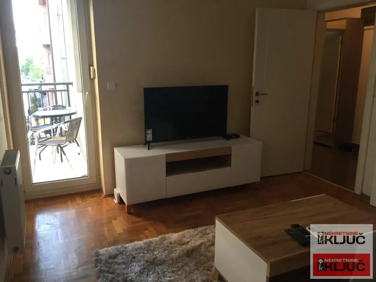 Dnevna soba sa televizorom, komodom i izlazom na terasu.