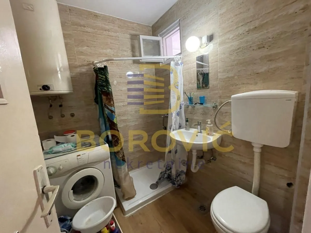 Manje kupatilo sa tuš kabinom, umivaonikom, WC šoljom i mašinom za veš.