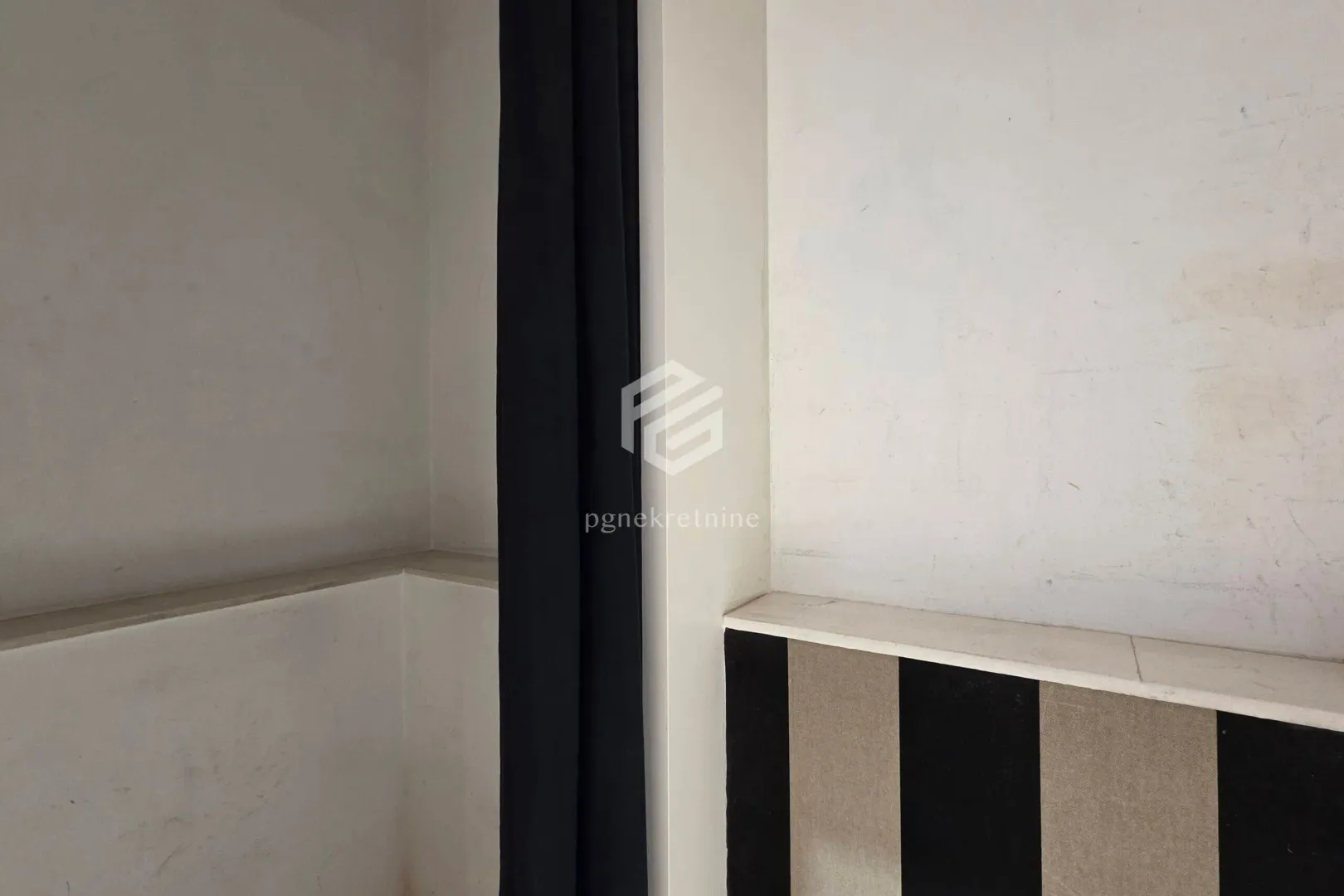 Detail of the interior space with white walls and a dark curtain.