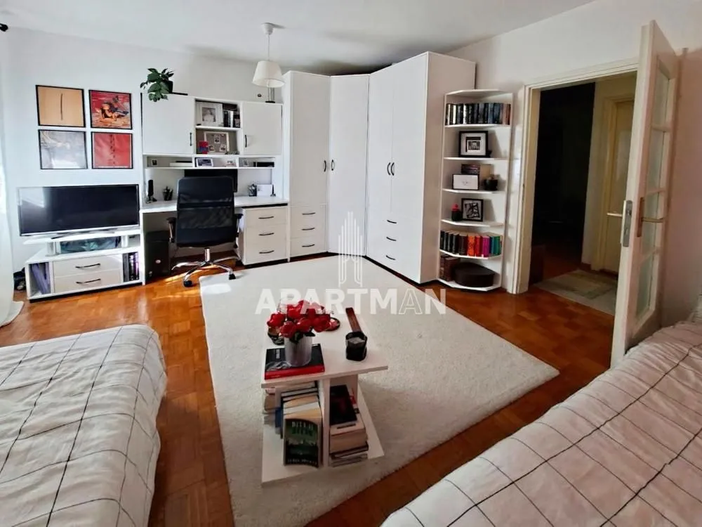 Dnevna soba sa krevetima, radnim stolom i belim ormarima.