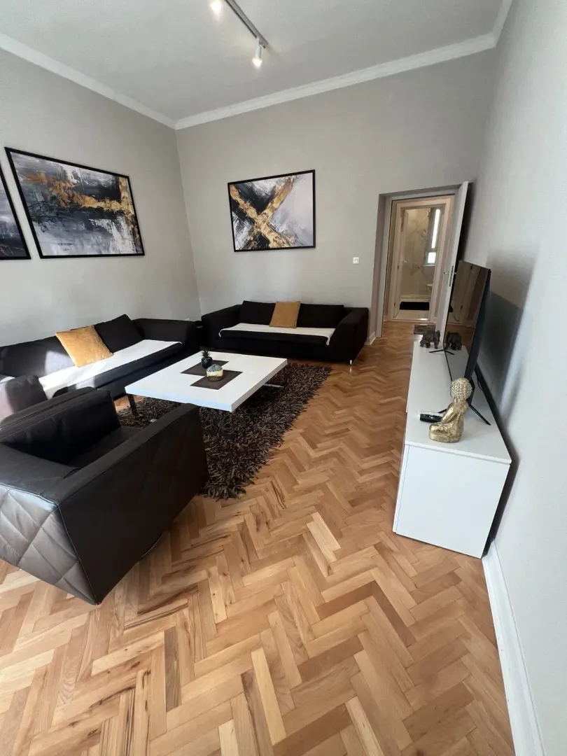 Bright living room with dark sofas and wooden parquet flooring.