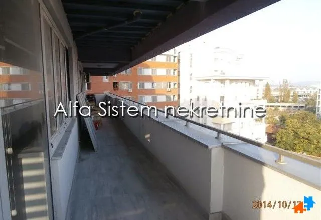 Dugačak natkriveni balkon sa pogledom na okolne zgrade.