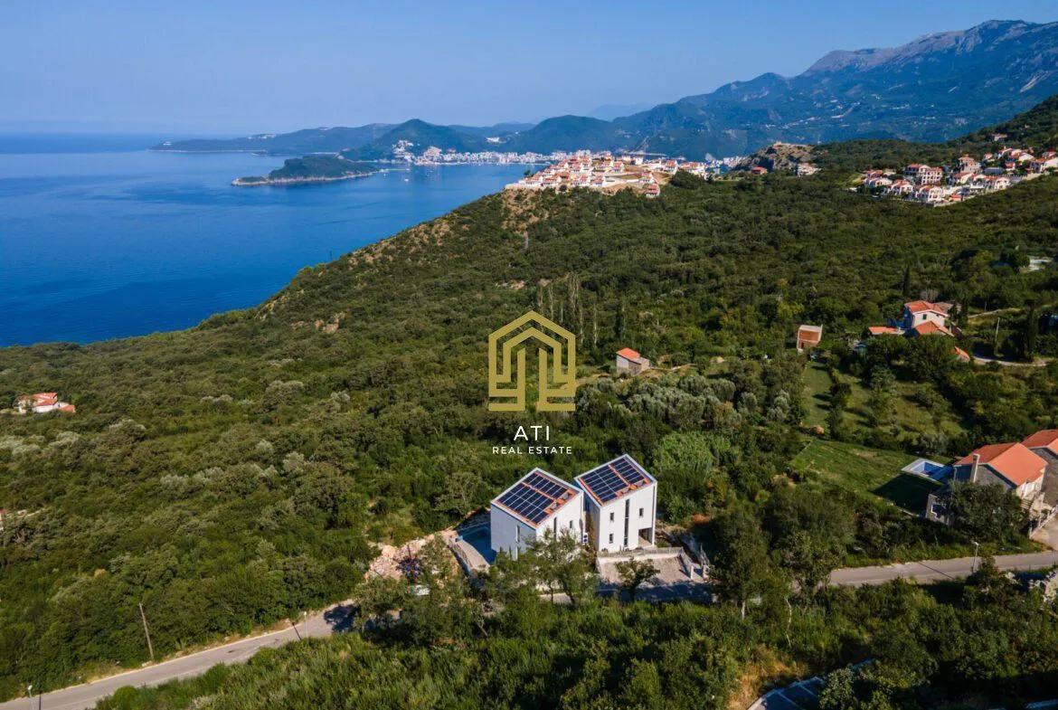 Pogled iz vazduha na kuće sa solarnim panelima i morskom obalom u pozadini.