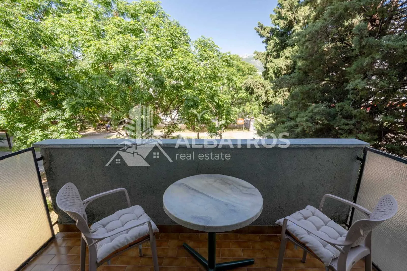 Manji balkon sa stolom i dve stolice i pogledom na zelenilo.