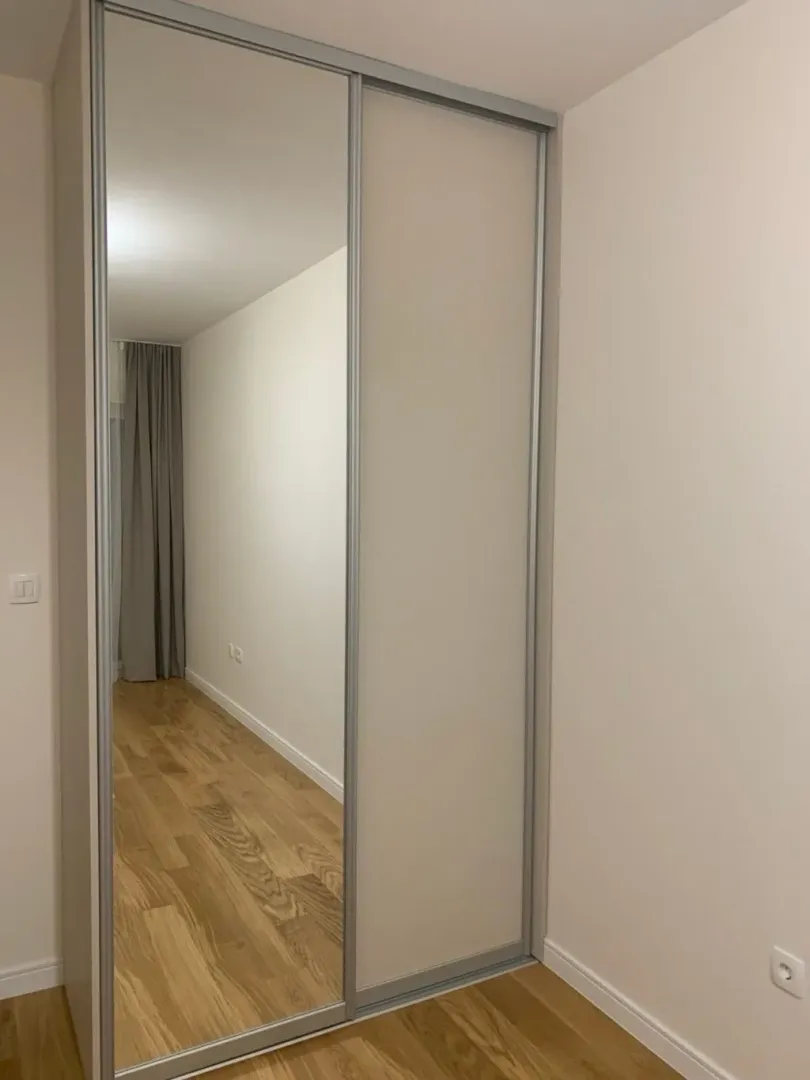 Bedroom with a mirrored built-in wardrobe and wooden flooring.