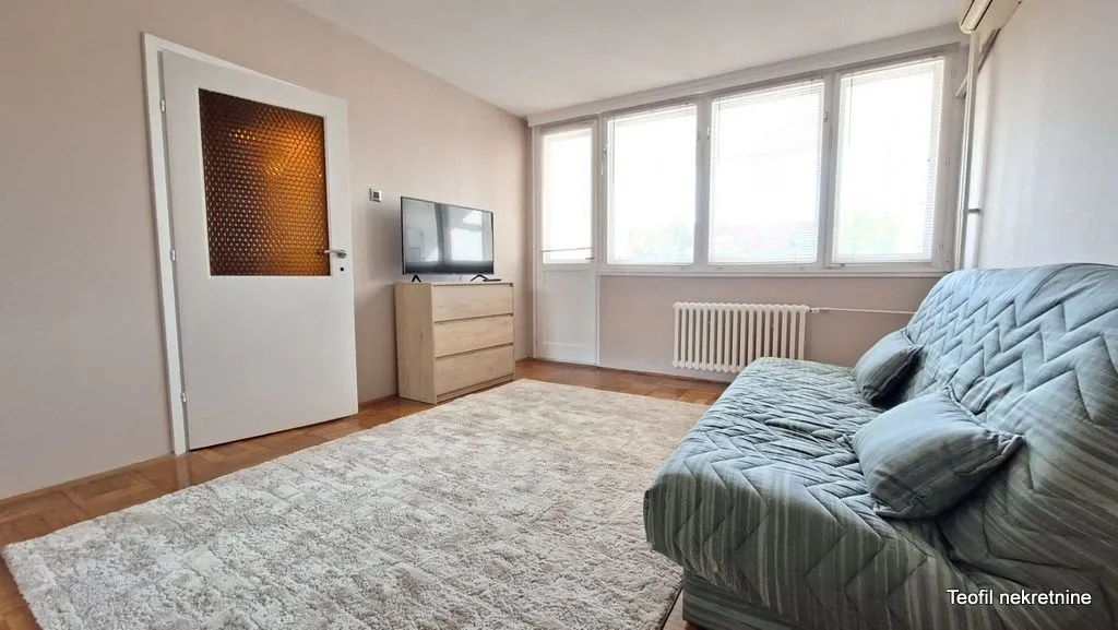 Living room with a sofa, chest of drawers, television, and large window.