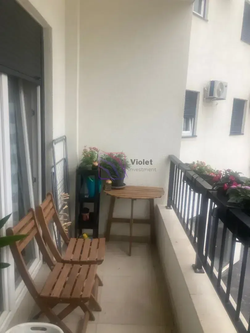 Manji balkon opremljen drvenim stolicama, stolom i cvijećem.