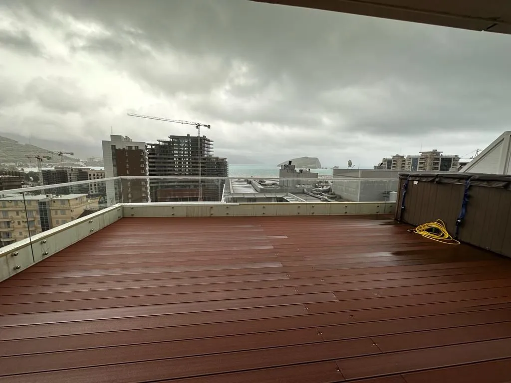 Spacious rooftop terrace with wooden decking and a view of the city and sea.