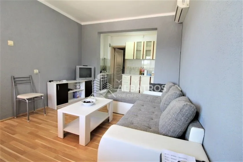 Living room with a corner sofa, coffee table, and television, overlooking the kitchen.